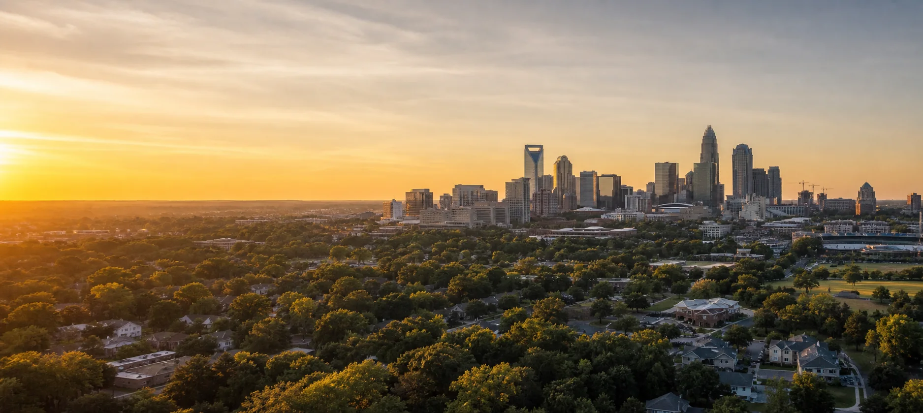 Charlotte skyline above leafy neighborhoods at golden hour